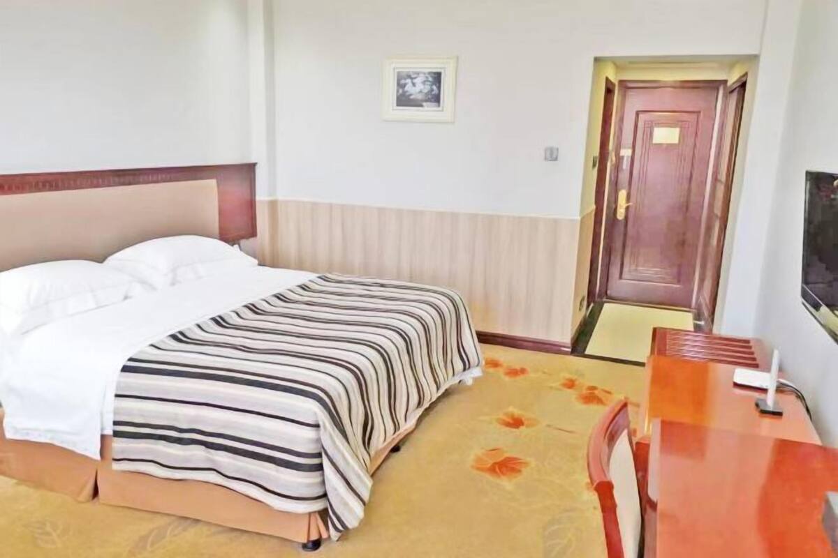 A hotel room with a bed, a wooden desk, a chair, a door, and a framed picture on the wall.