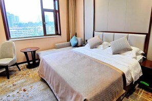 A hotel room with a large bed, a chair, a small table, and a view of the city through a large window. - Yang Quan Hotel (Yangquan)