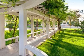 A covered outdoor seating area with benches, surrounded by grass and trees. - Yang Quan Hotel (Yangquan)