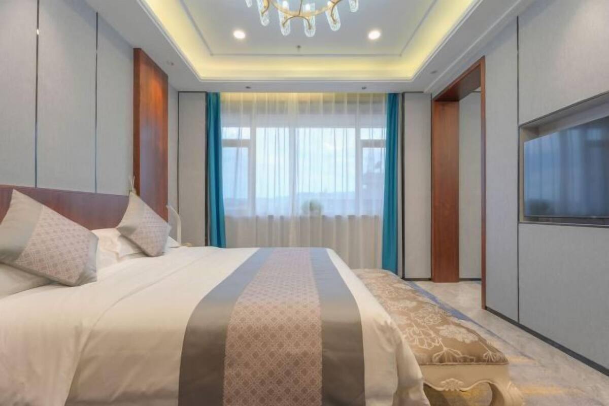 A modern bedroom with a large bed, a TV, and a chandelier.