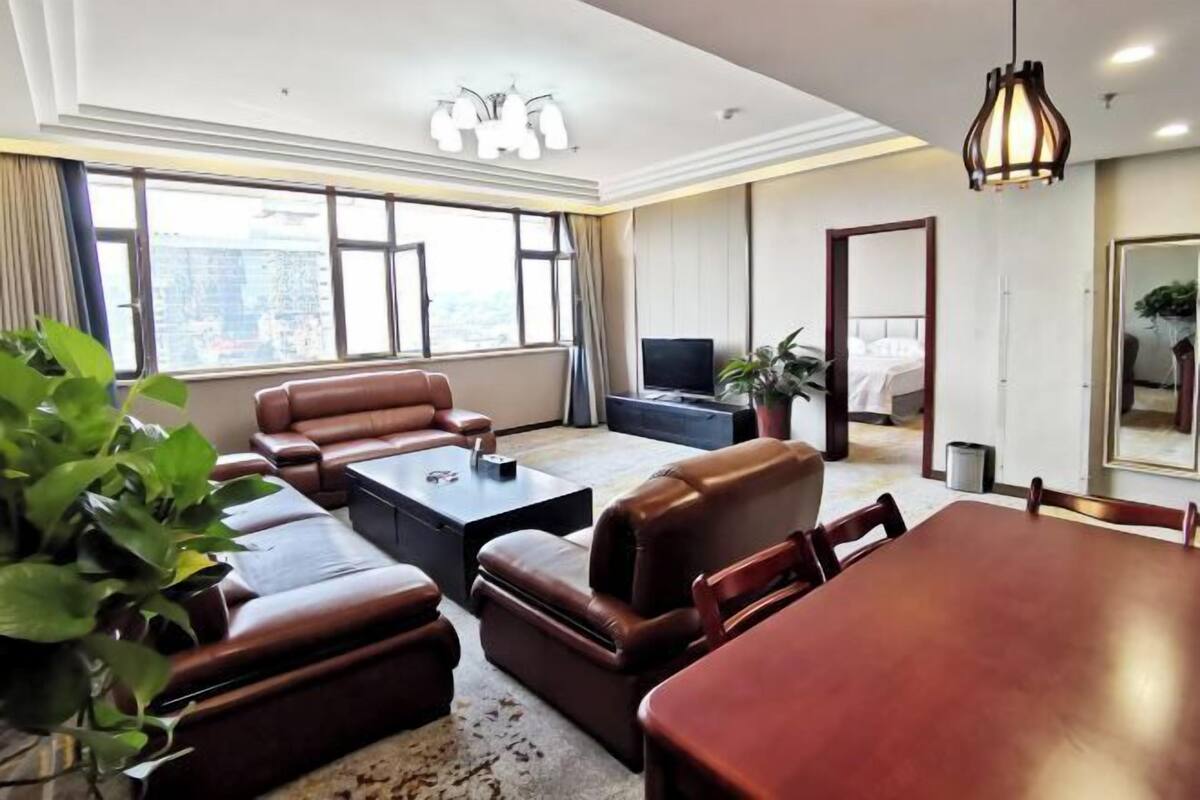 A modern hotel room with leather sofas, a dining table, a flat-screen TV, and large windows.