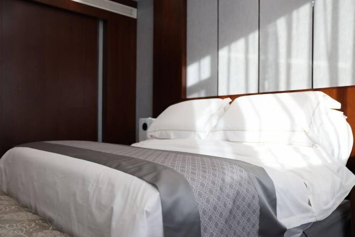 A hotel room with a bed, a wooden wardrobe, and a window allowing natural light.