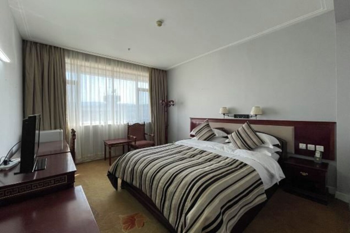 A hotel room with a bed, a desk, a chair, a television, and a window with curtains.