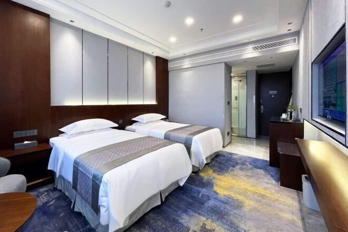 A hotel room with two beds, a desk, a chair, a TV, and a large mirror.