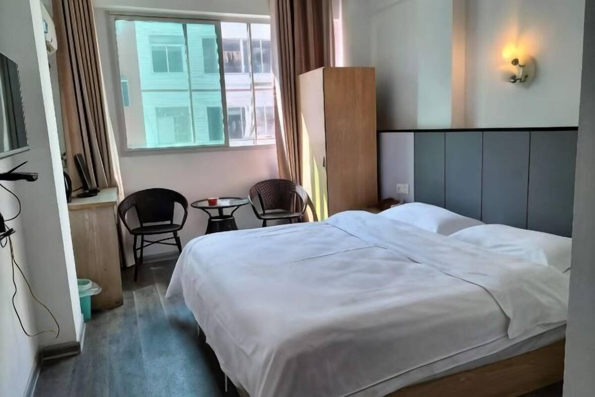 Ein Hotelzimmer mit einem Bett, einem Schreibtisch, zwei Stühlen, einem Kleiderschrank und einem Vorhangfenster.