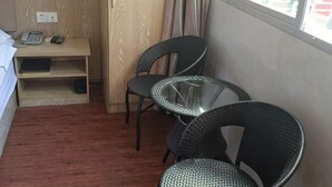 Habitación de hotel con una cama, un escritorio con teléfono, dos sillas, una mesita de vidrio y una ventana.