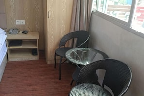 Una camera d'albergo con un letto, una scrivania con il telefono, due sedie, un tavolino in vetro e una finestra.