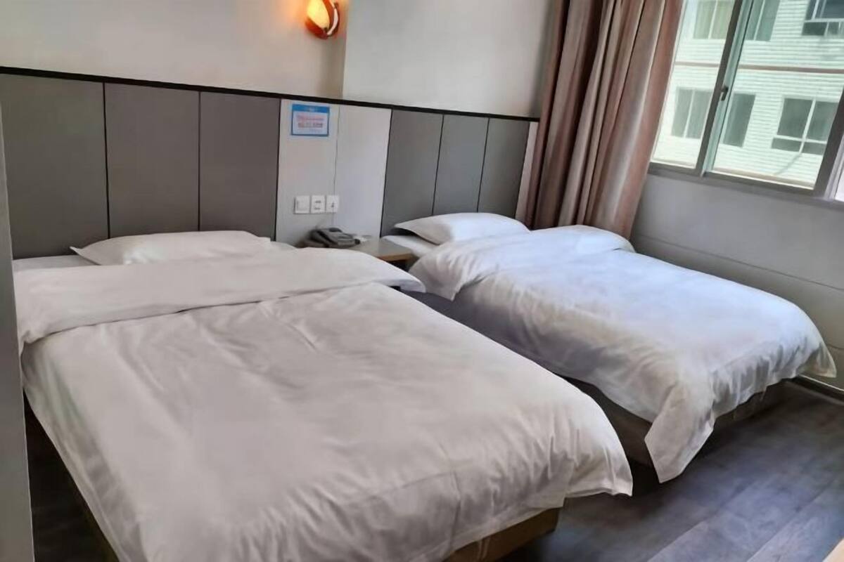 Ein Hotelzimmer mit zwei Betten, einem Nachttisch, einer Wandleuchte und einem Fenster mit Vorhängen.