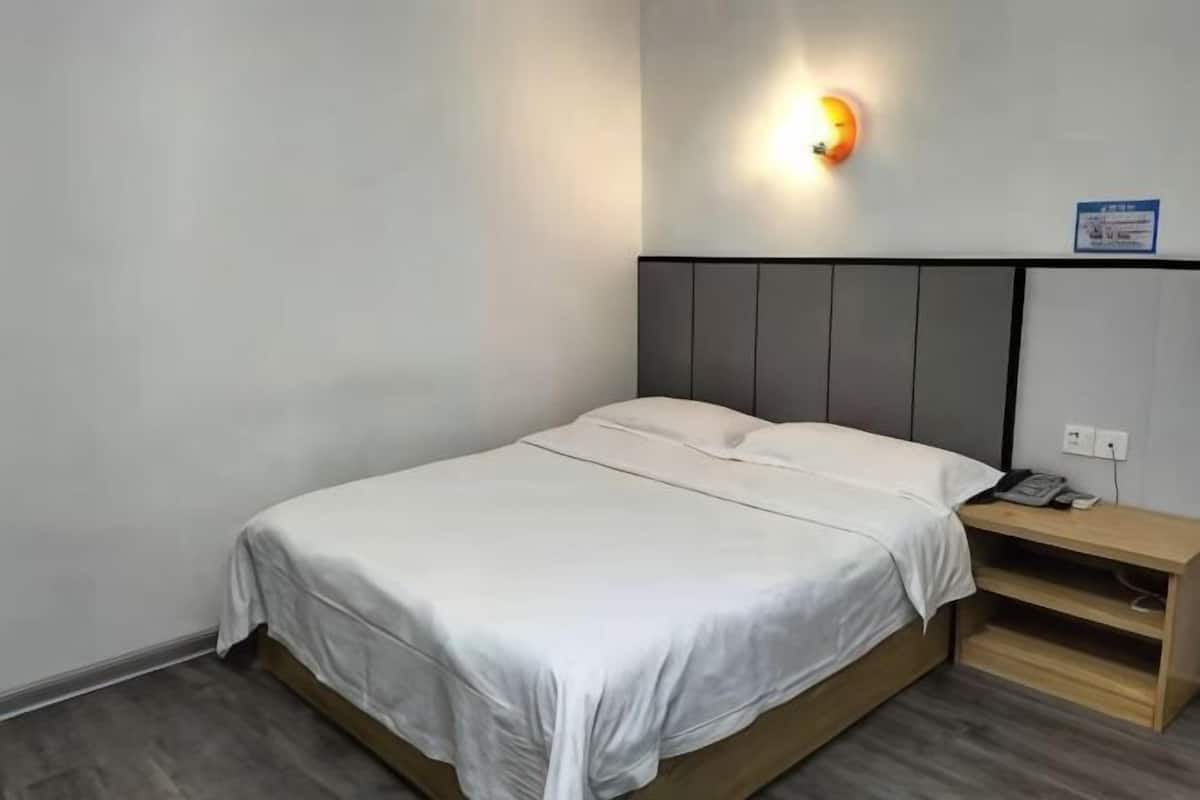 A single bed with a wooden frame, a nightstand, and a wall-mounted light fixture.