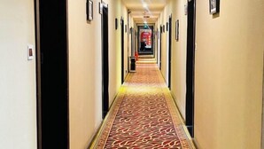 A hotel hallway with a patterned carpet, doors on both sides, and a red sign in the distance. - Xiangbala Hotel (Muli)