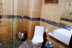 A bathroom with a glass shower enclosure, a toilet, and a sink. - Xiangbala Hotel (Muli)