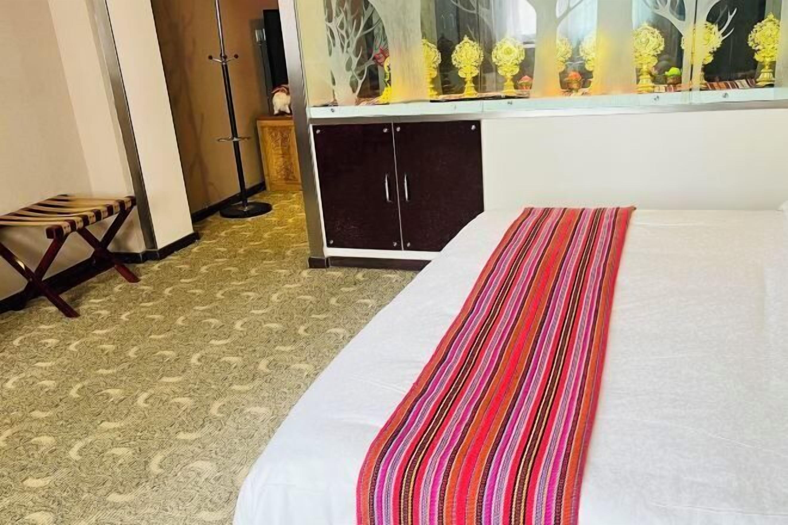 Habitación de hotel con una cama, un pequeño banco de madera, un armario y un ventanal decorado con flores.