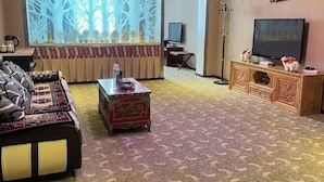 A living room with a sofa, a coffee table, a television, and a decorative screen. - Xiangbala Hotel (Muli)