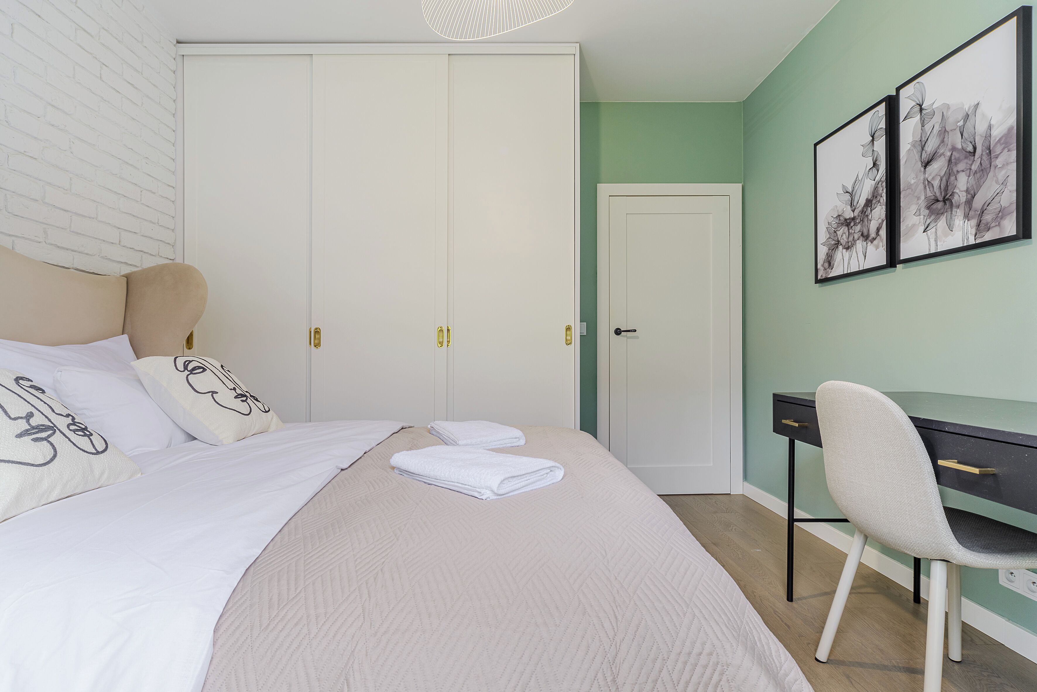 A bedroom with a bed, a desk, and a chair. There are two doors, one with a white frame and another with a black frame.