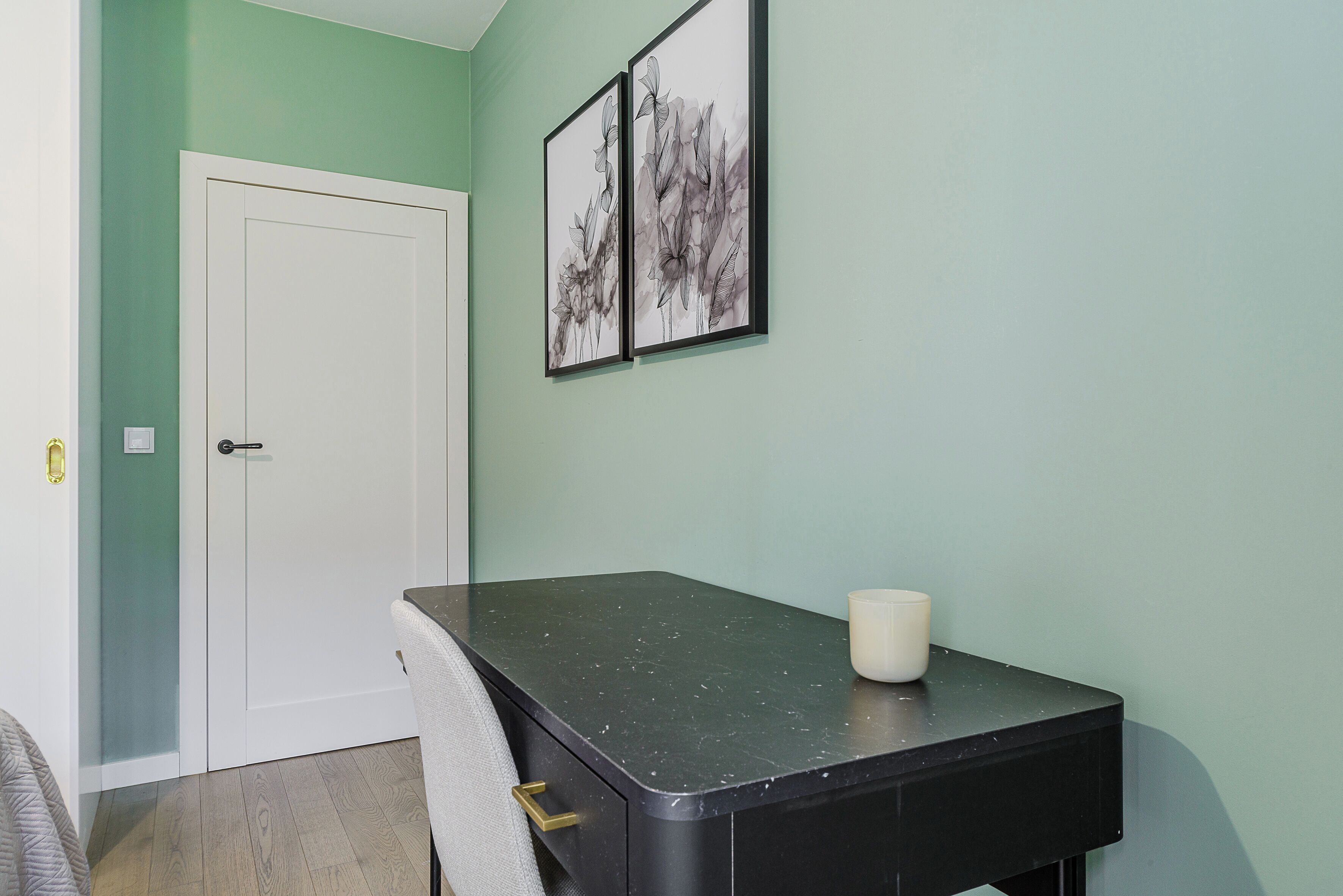 Une pièce avec une porte blanche, une table noire sur laquelle se trouve un objet blanc, et deux tableaux encadrés accrochés au mur.