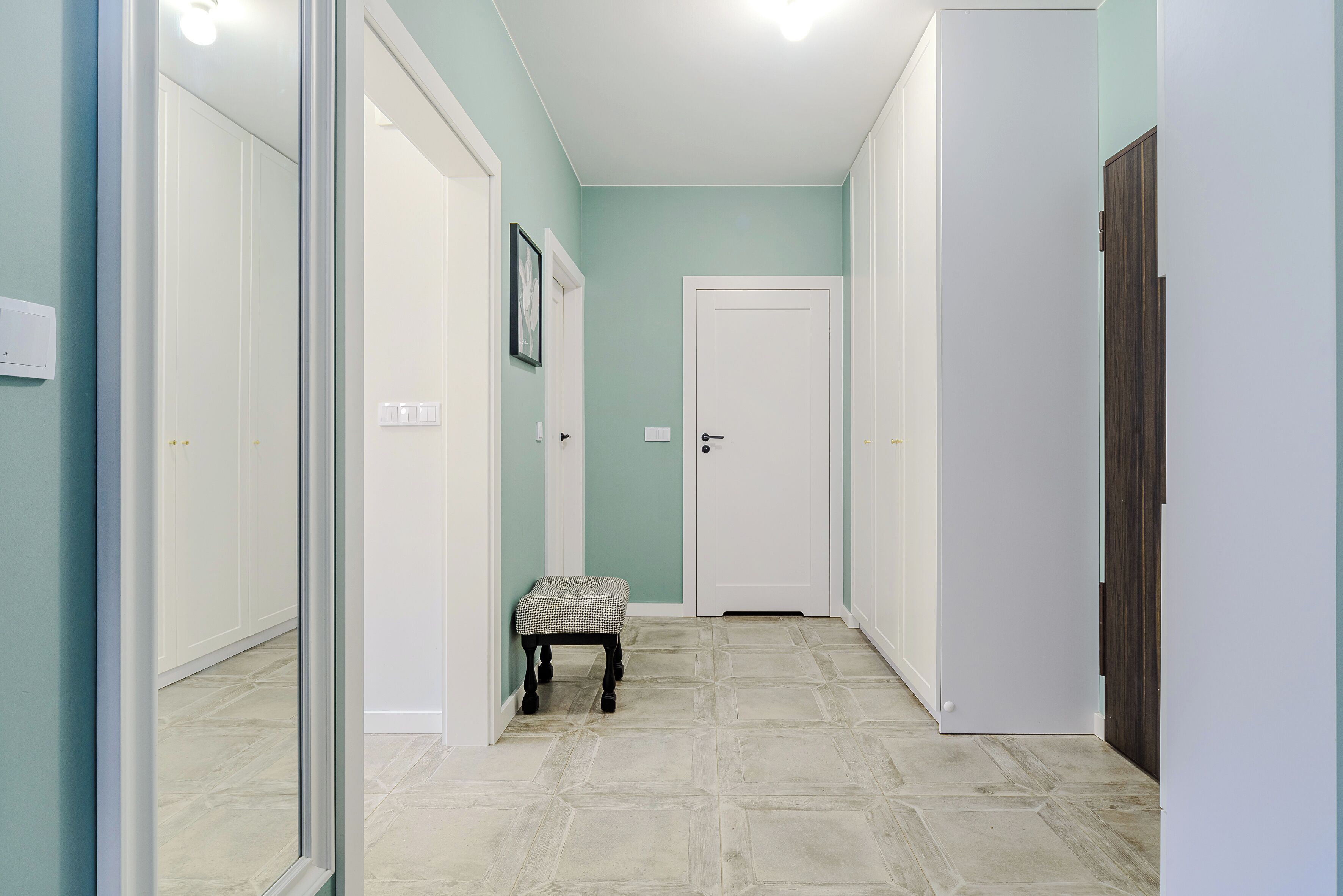 A hallway with a checkered bench, white doors, and a light teal wall.