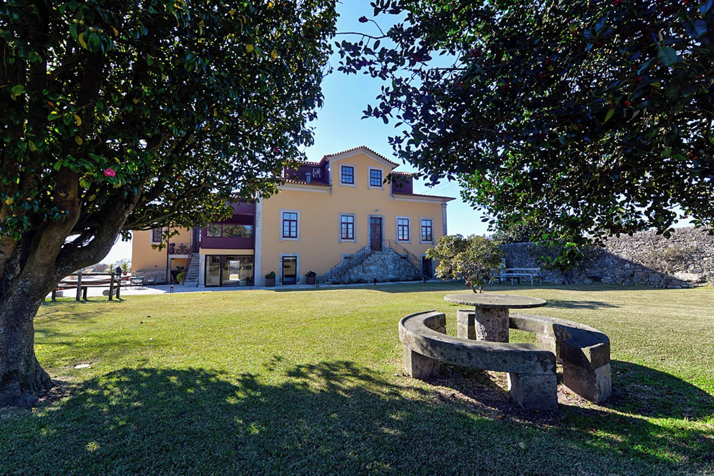 A building with a yellow facade, a stone staircase, and a grassy lawn with a circular stone bench.