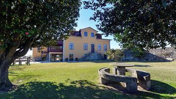 A building with a yellow facade, a stone staircase, and a grassy lawn with a circular stone bench.