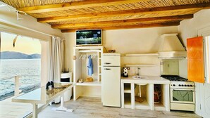 Cocina compacta con techo de madera, televisor sobre el lavamanos y vista al mar a través de un ventanal grande.