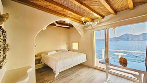 Un dormitorio con cama, ventana con vista al mar y techo de madera.