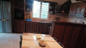 A kitchen with a wooden table, chairs, and a refrigerator. - 4-bedroom house for 10 people (L'Étang-Salé)