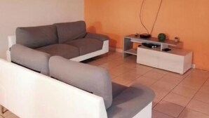 A living room with a grey sofa, a white coffee table, and a TV mounted on the wall. - 4-bedroom house for 10 people (L'Étang-Salé)