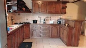 A kitchen with wooden cabinets, a stove, and a tiled floor. - 4-bedroom house for 10 people (L'Étang-Salé)