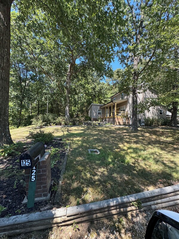 A residential area with a mailbox labeled 125, surrounded by trees and a house with a porch.