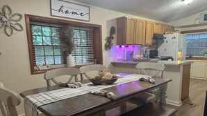 A dining area with a wooden table, chairs, and a bench. There is a window with blinds, a decorative wall piece, and a sign above the table. - Water view 3-bedroom house in Camden with AC and WiFi walking distance to lake (Camden)