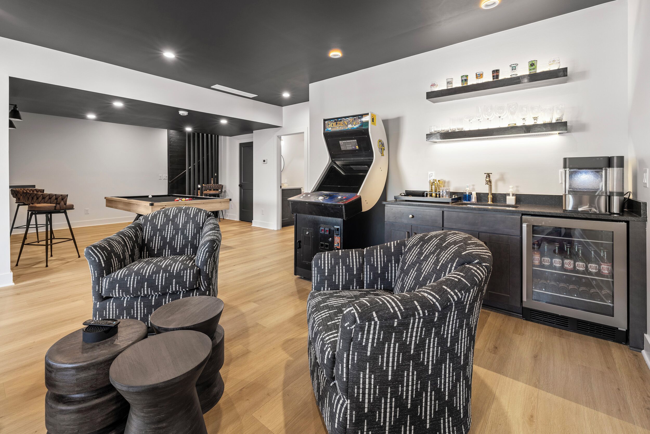 Un espace de détente moderne comprenant une table de billard, des sièges confortables, un juke-box et un réfrigérateur rempli de boissons.