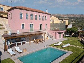 Una villa rosa con piscina, mobiliario de exterior y vistas al campo.