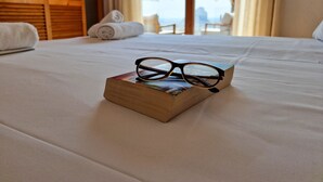 A neatly made bed with a pair of glasses on a book, a rolled towel, and a view of the ocean through large windows. - A021 - COLINA DEL SOL (Calpe)