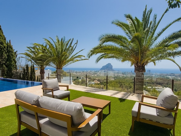 Relax in style with a clear view of the city and ocean from this outdoor seating area, featuring a pool and comfortable seating for two.