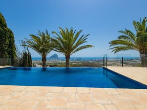 Relax by the serene pool surrounded by lush palm trees and a stunning coastal cityscape.
