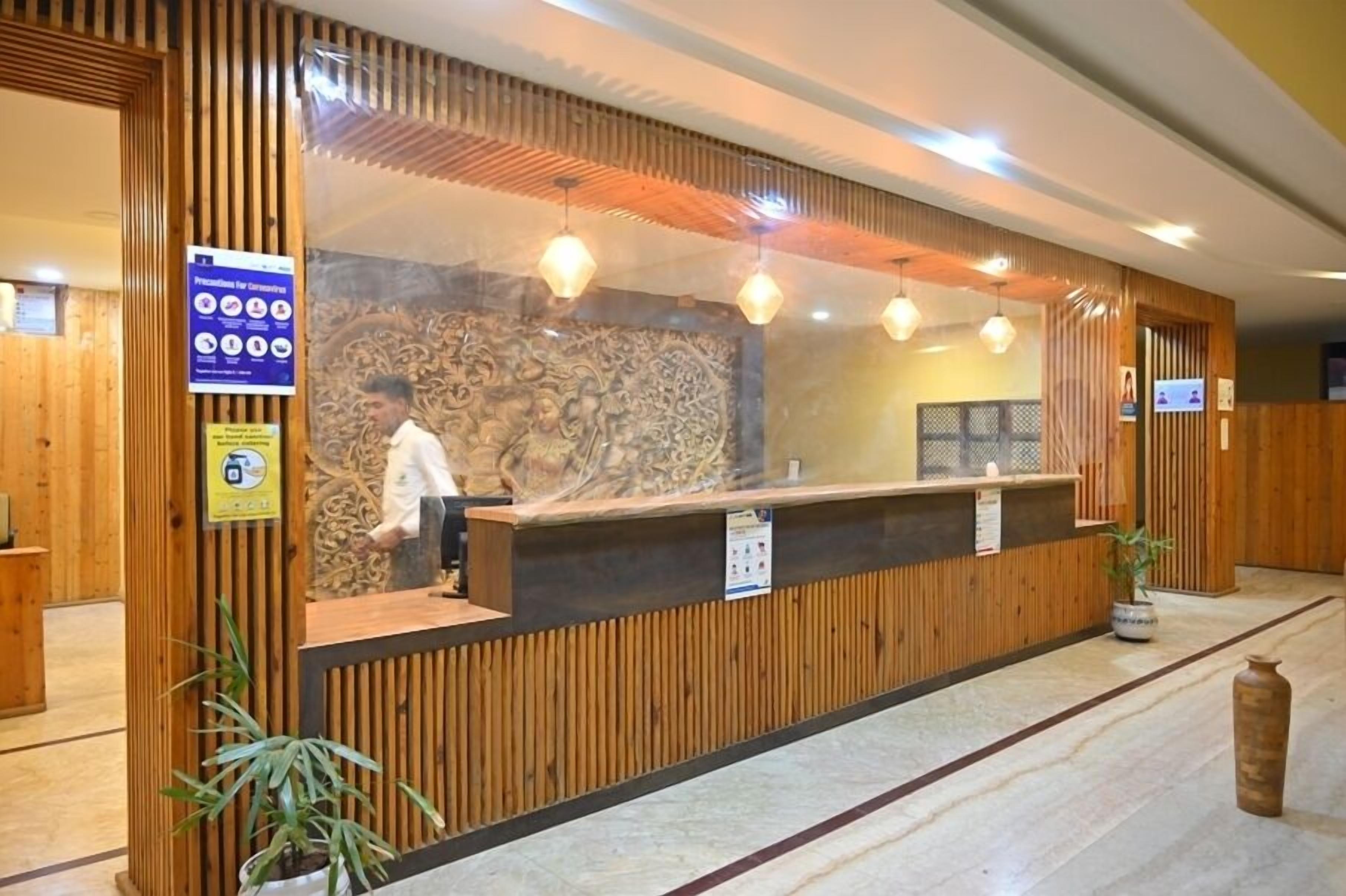 Una zona de recepción con un mostrador de madera, una pared de piedra con detalles tallados y una persona de pie detrás del mostrador.