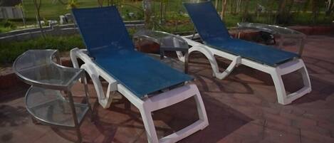 Sillones de exterior con mesitas de vidrio en un patio empedrado.