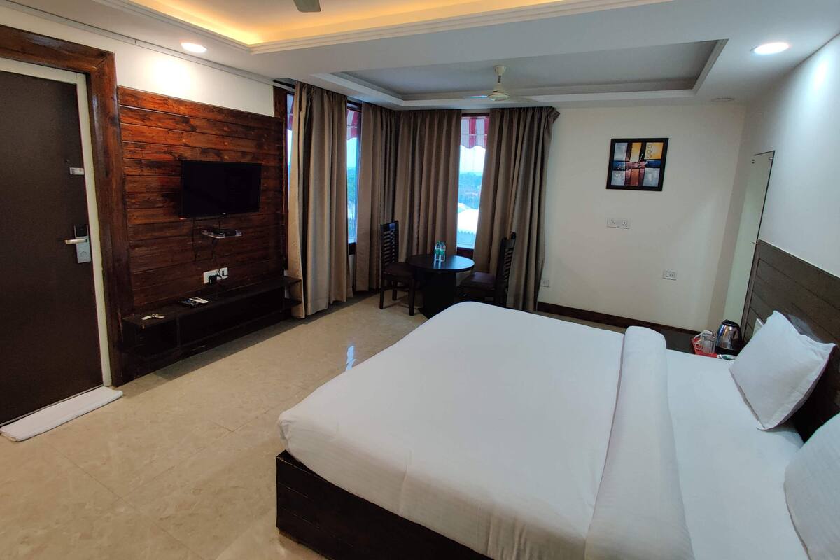 Ein Hotelzimmer mit einem großen Bett, einem an einer Holzwand montierten Fernseher, einem Esstisch mit Stühlen und einem Deckenventilator.
