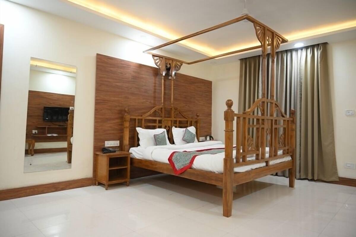 Ein Himmelbett mit Holzrahmen und Baldachin, ein Nachttisch, ein Spiegel und ein Fernseher auf einem Standfuß.