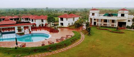 A resort with a swimming pool, multiple buildings with red-tiled roofs, and a well-maintained lawn.