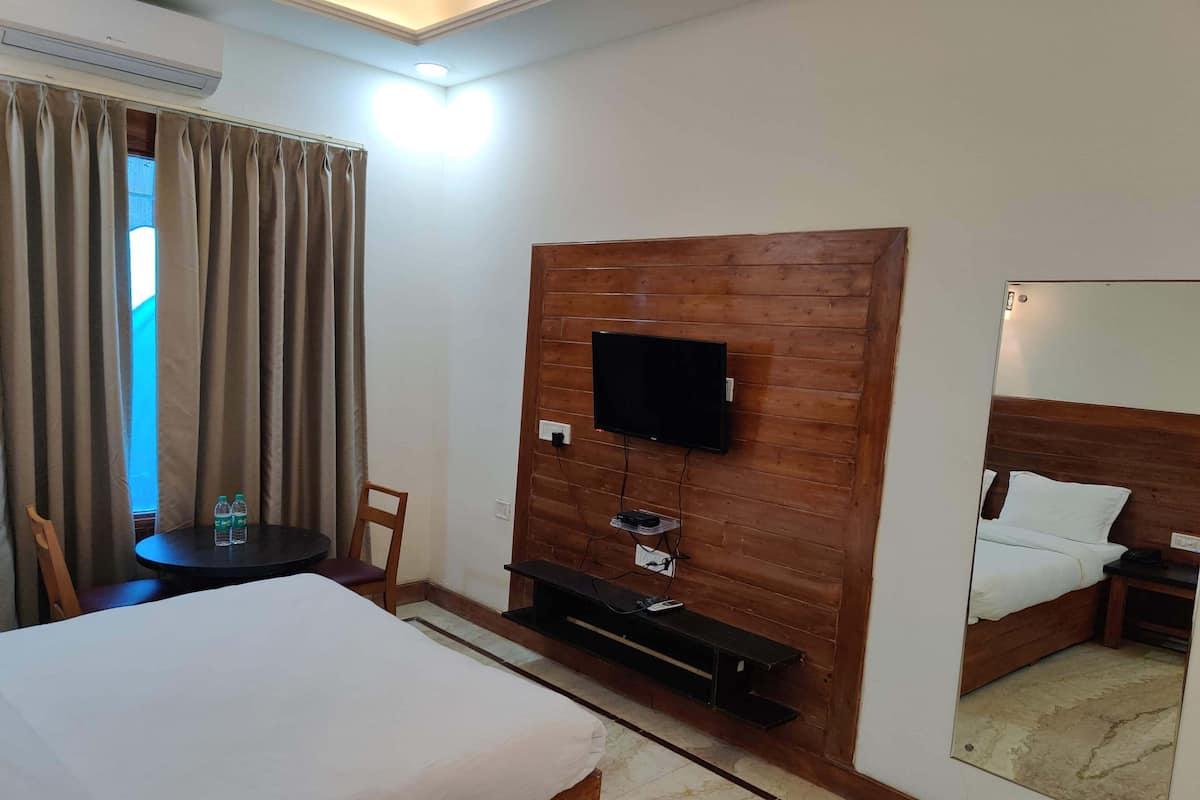 Ein Hotelzimmer mit einem Bett, einem an einer Holzwand montierten Fernseher, einem kleinen Tisch mit zwei Flaschen, einem Sessel und einem Spiegel, der das Bett und einen Nachttisch reflektiert.