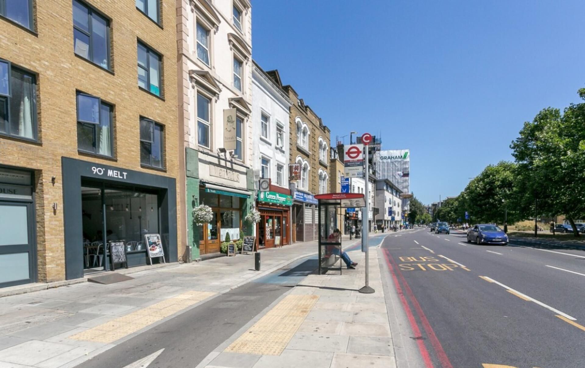 A street view with a bus stop, shops, and a clear road.