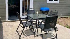 Una veranda con tavolo e sedie, un barbecue blu e una porta scorrevole che dà su una stanza.