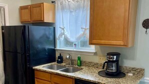 Una cucina compatta con ripiani in granito, mobili in legno, frigorifero nero, macchina del caffè e lavastoviglie.