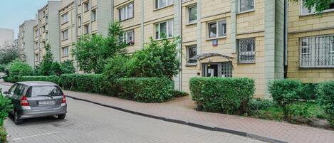 A multi-story residential building with a paved driveway and green hedges.
