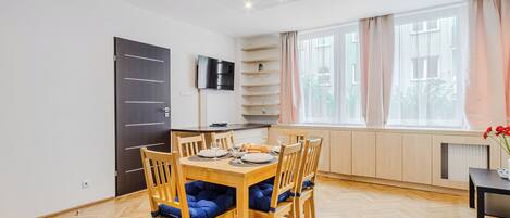 Un coin repas avec une table et des chaises en bois, un téléviseur fixé au mur et une fenêtre avec des rideaux.