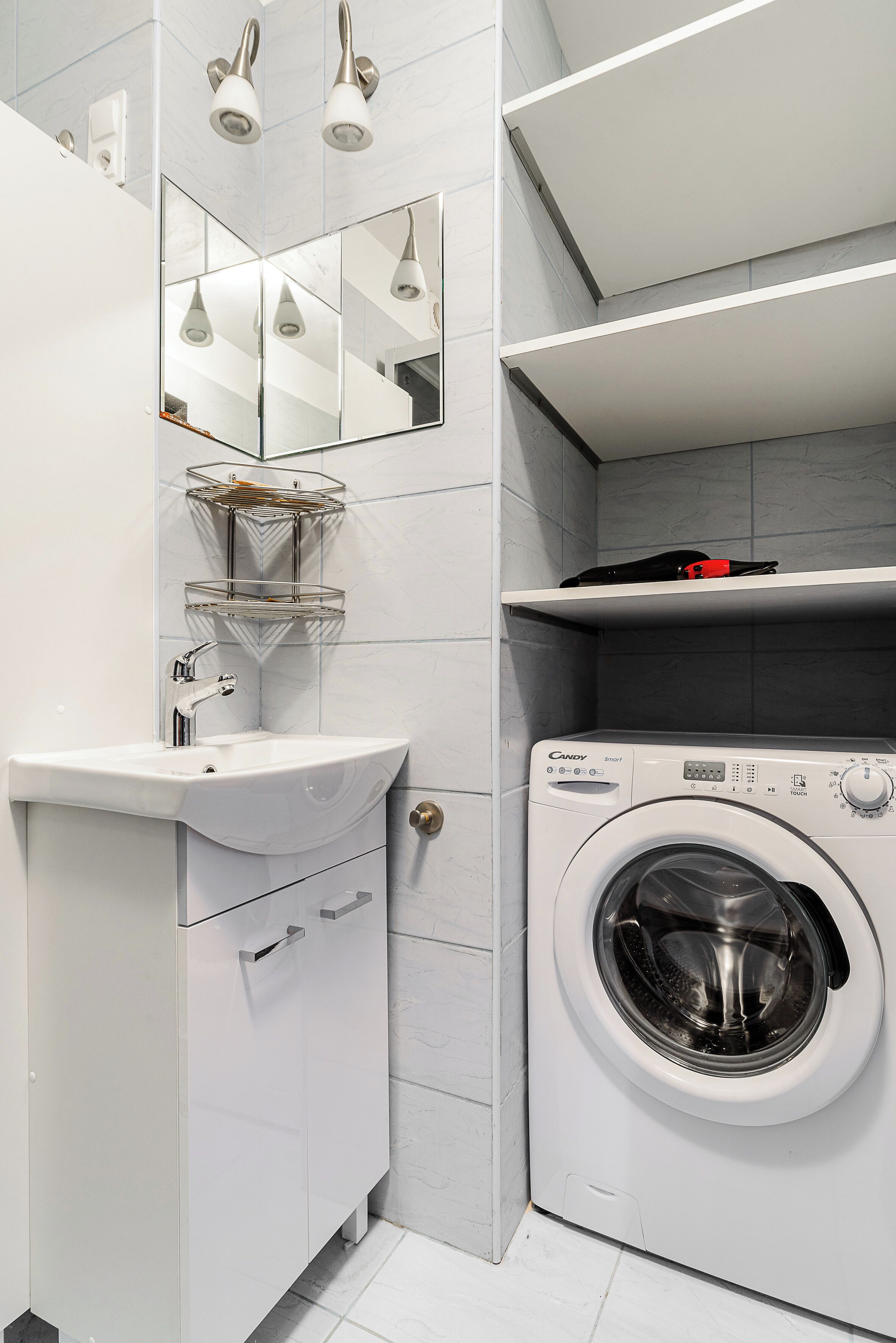 Un baño moderno con lavamanos blanco, espejo y lavadora integrada.