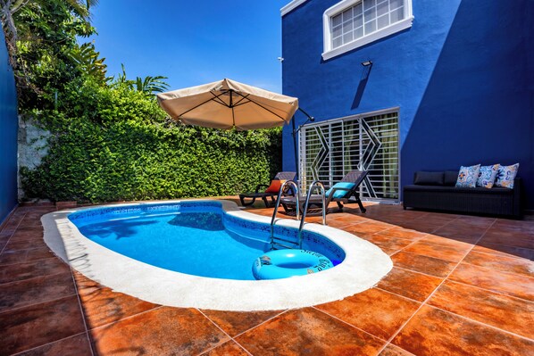 A swimming pool with a white edge, a lounge area with a sofa and chairs, and a blue wall.