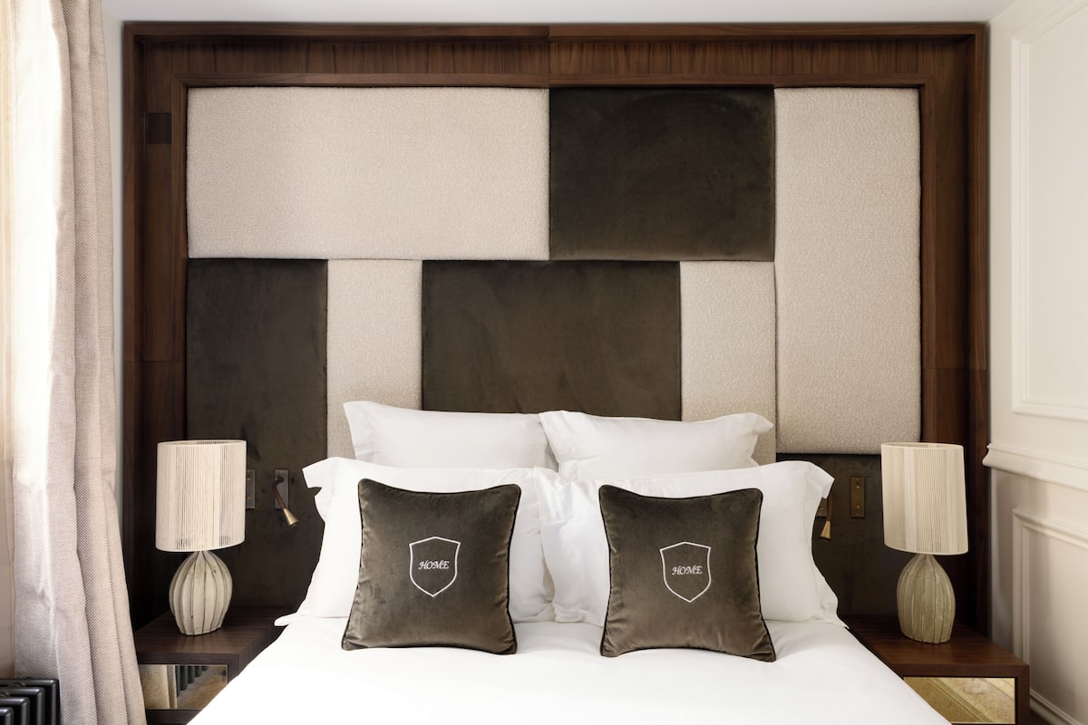 A neatly made bed with white linens and two pillows with a house emblem, flanked by two bedside lamps on wooden nightstands.