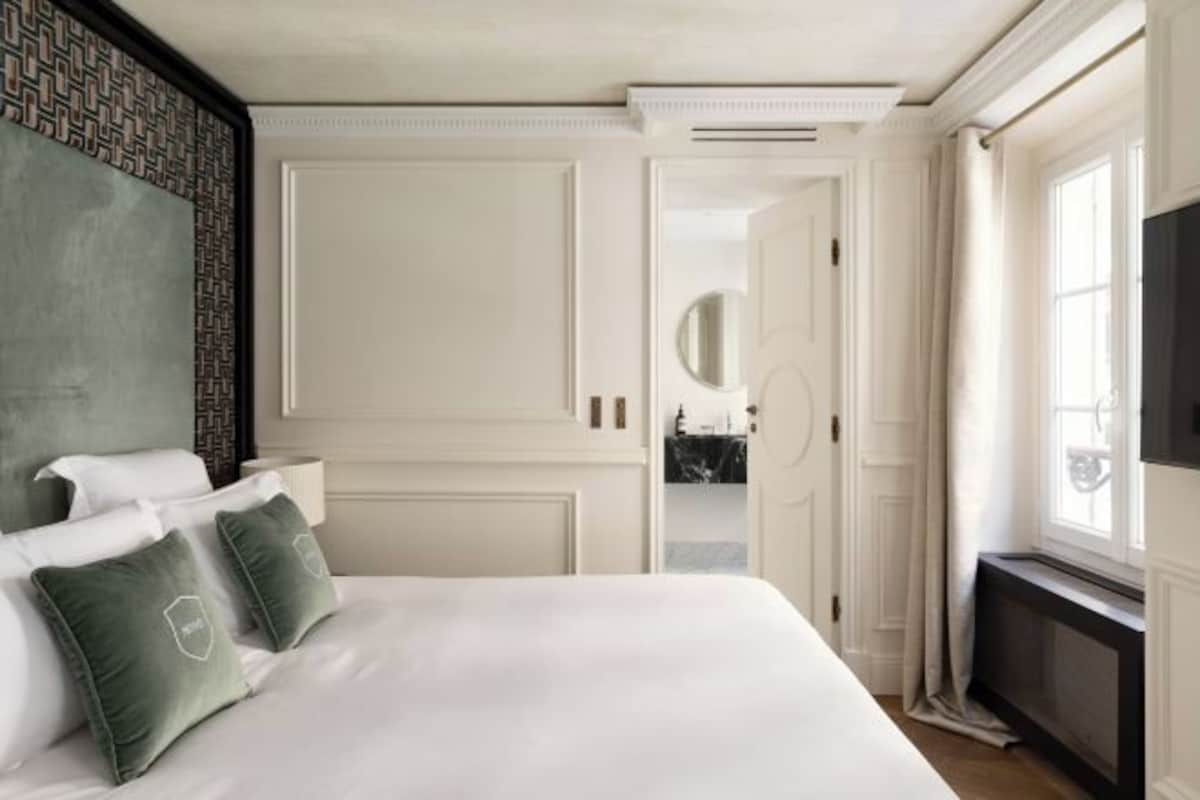 A hotel room with a large bed, a television, a mirror, and a view of the hallway.