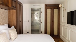 Habitación de hotel con una cama grande, armario de madera, televisor y baño con espejo y lavamanos.